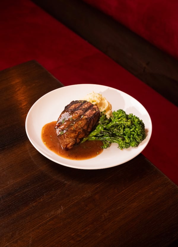 A plate with a filet mignon steak in a pool of sauce with a side of broccolini next to it.