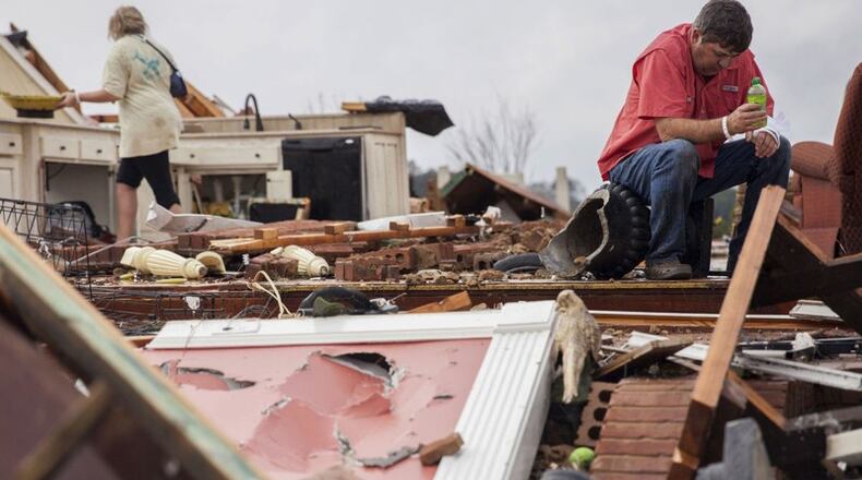 Jeff Bullard sits in what used to be the foyer of his home as his daughter, Jenny Bullard, looks through debris at their home that was damaged by a tornado Sunday in Adel. Gov. Nathan Deal declared a state of emergency in 16 counties. (Credit: Branden Camp / Associated Press)
