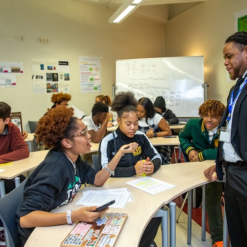 Kelsey Allen (front left) talks with her teacher, Rashad Brown, in their advanced placement African American studies class at Maynard Jackson High School. Students debate why other states are restricting the course. (Jenni Girtman for the AJC 2023)