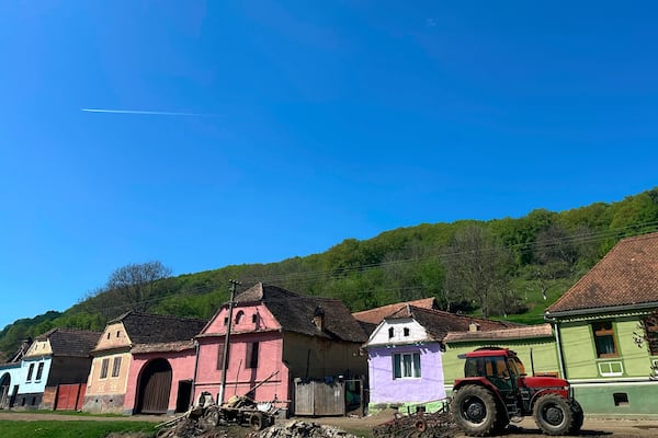 A tractor is parked outside a row of houses in the village of Floresti, in Romania's central Transylvania region, Thursday, April 24, 2025. (AP Photo/Stephen McGrath)