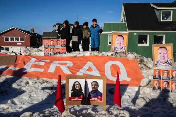 Children stand in the snow as candidate's pictures on boards are seen outside a polling station during parliamentary elections, in Nuuk, Greenland, Tuesday, March 11, 2025. (AP Photo/Evgeniy Maloletka)