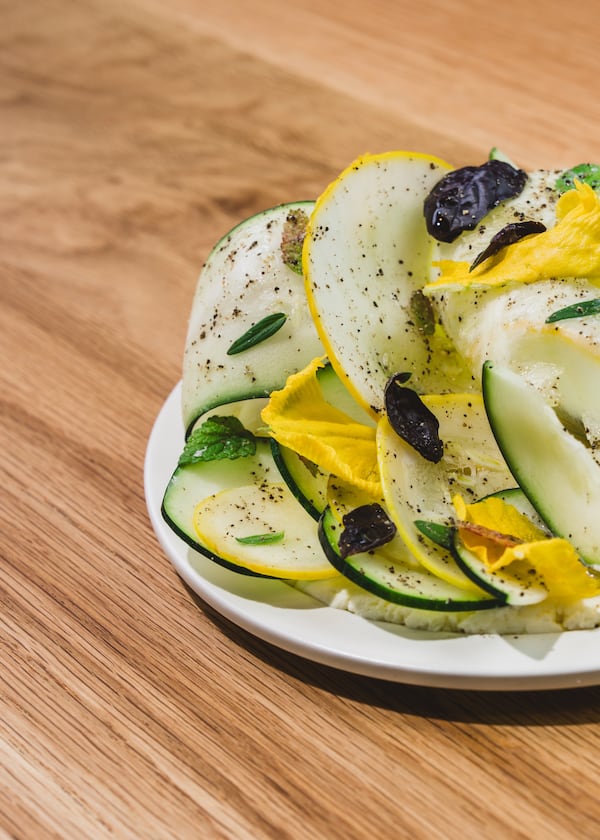 Half of a plate extends into frame from the right, with ribbons of squash arranged in layers on top of a bed of white cheese.