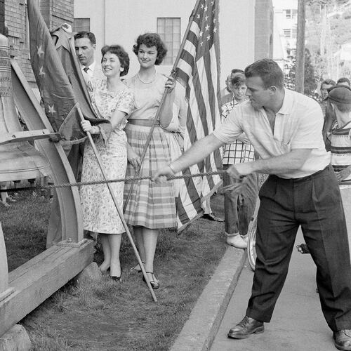 FILE - Romer Derr rings a replica of the Liberty Bell outside the Federal Building 49 times, signifying Alaska's joining the United States as the 49th state, on July 1, 1958, in Juneau, Alaska. Behind Derr holding the Alaska flag, left, is Judy Findlay and holding the U.S. flag, right, is Marilee Nowacki. (AP Photo/JK, File)