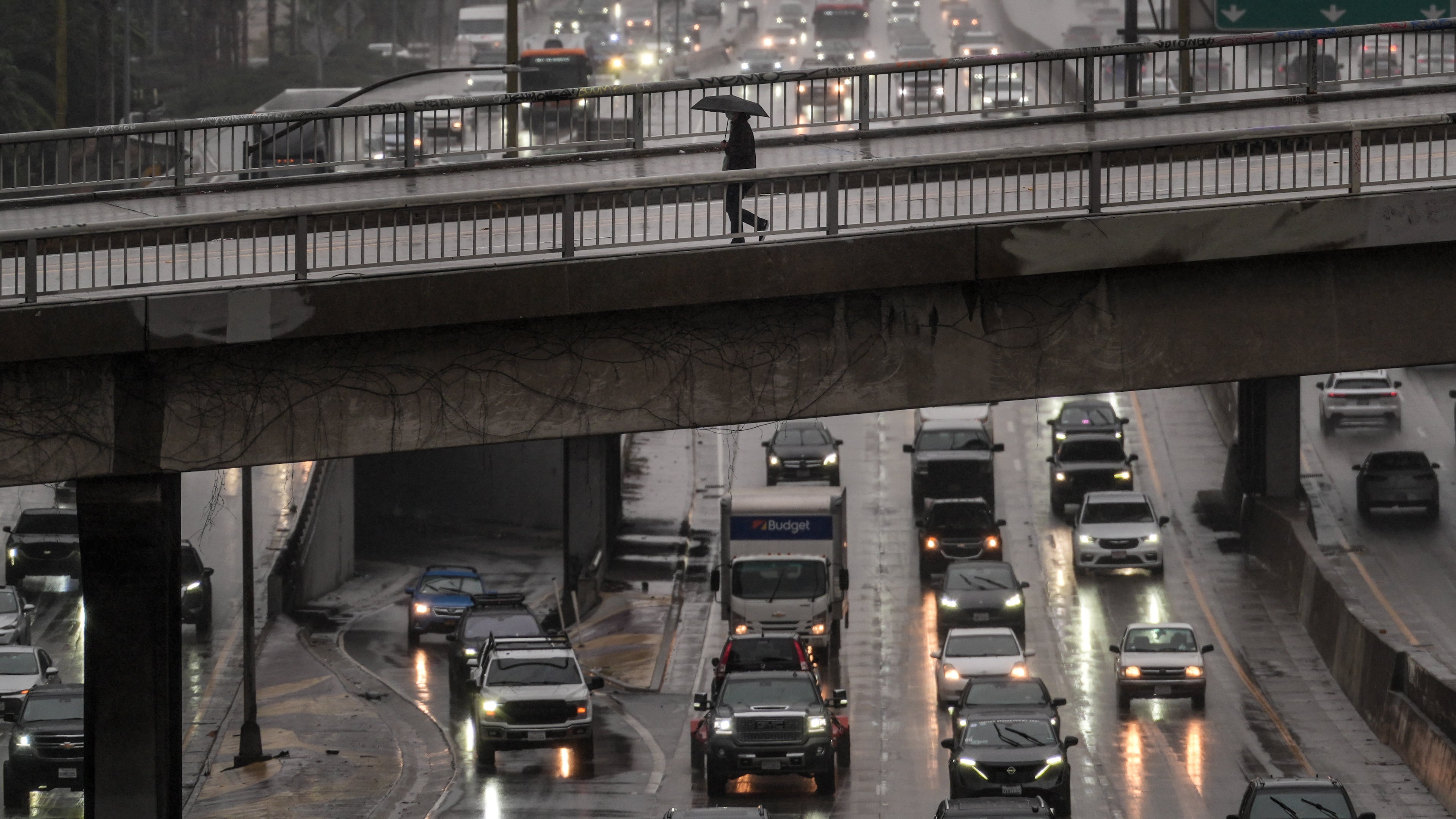 A pedestrian with an umbrella walks on a bridge over the rain-soaked 110 Freeway in Los Angeles Friday, Nov. 14, 2025. (AP Photo/Jae C. Hong)