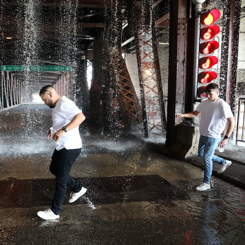 People scamper west across the lower level of the DuSable Lake Shore Drive bridge over the Chicago River on Wednesday, Sept. 2, 2026, as water pumped by a Chicago Fire Department boat flows down onto the double-leaf, double-deck, fixed counterweight bridge. (Terrence Antonio James/Chicago Tribune via AP)