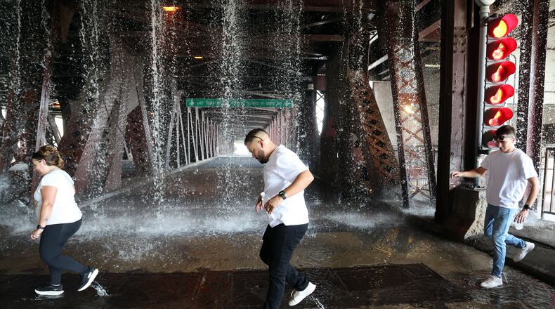 People scamper west across the lower level of the DuSable Lake Shore Drive bridge over the Chicago River on Wednesday, Sept. 2, 2026, as water pumped by a Chicago Fire Department boat flows down onto the double-leaf, double-deck, fixed counterweight bridge. (Terrence Antonio James/Chicago Tribune via AP)