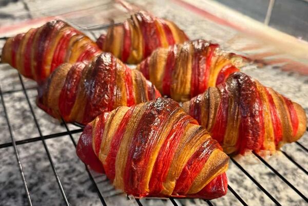 Six croissants are resting on a cooling rack. They are distinctive because their layers are two colors instead of the usual one color.