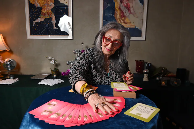 Healing practitioner Rolene Jaffe shows Rise & Radiate oracle cards, which Jaffe created, at 7th House, an astrological-themed restaurant where her son, Alexander Sher, is part owner, on Wednesday, April 1, 2026, in Atlanta. (Hyosub Shin/AJC)