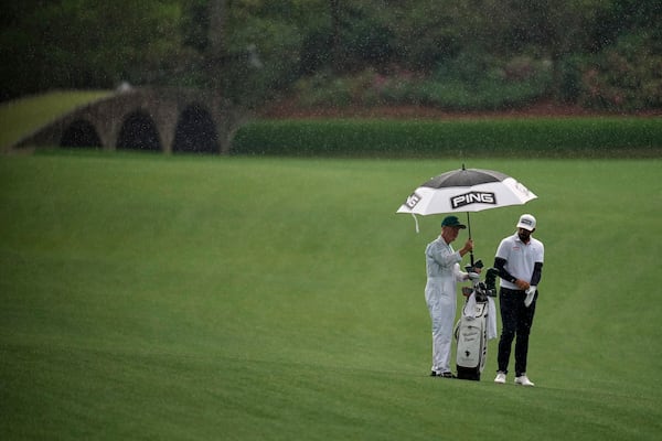 Matthieu Pavon, of France, keeps dry on the 13th fairway with caddie Mark Sherwood, left, during a practice round at the Masters golf tournament, Monday, April 7, 2025, in Augusta, Ga. (AP Photo/Ashley Landis)