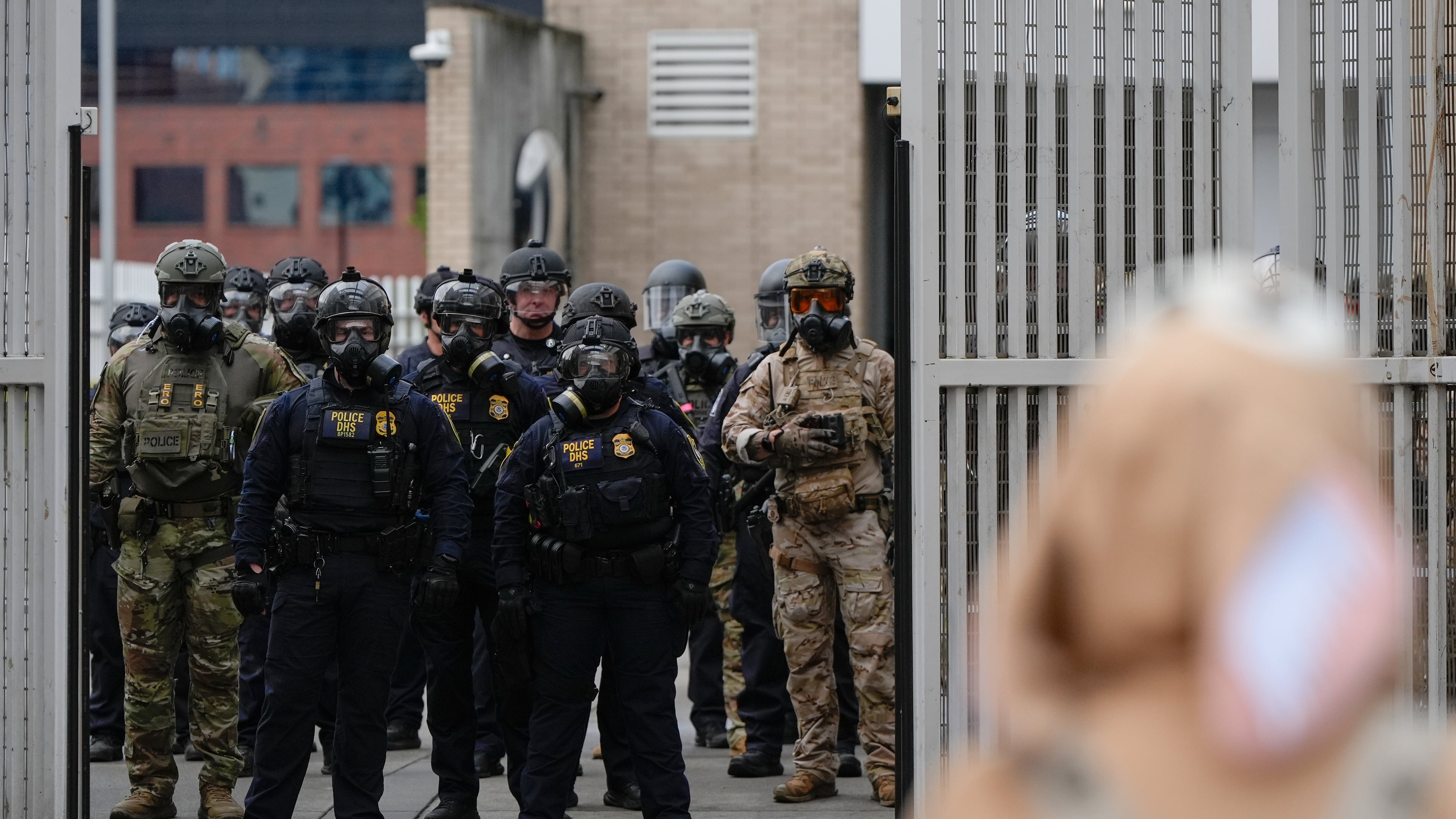 Law enforcement officers watch as the gates close at a U.S. Immigration and Customs Enforcement facility as people protest outside on Saturday, Oct. 11, 2025, in Portland, Ore. (AP Photo/Jenny Kane)
