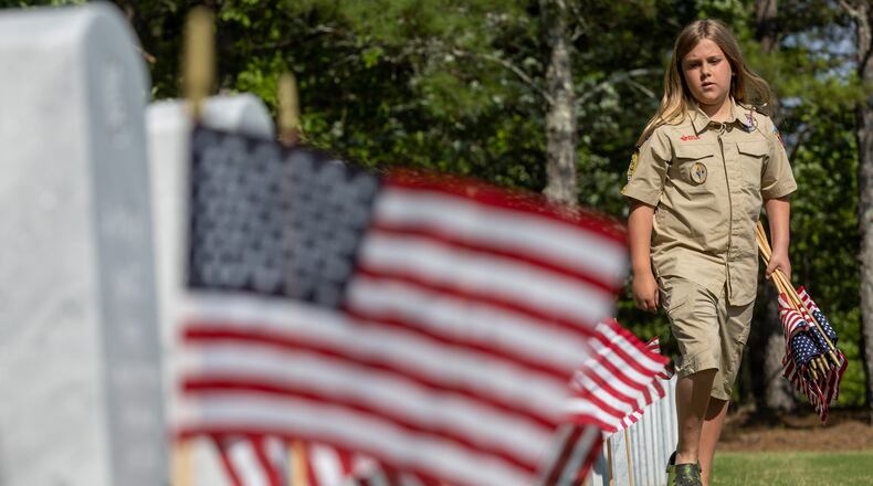 Karson Troville, with Troop 1755, places flags in front of tombstones at the Georgia National Cemetery in Canton Saturday, May 27, 2023. Volunteers will place an estimated 21,000 flags on tombstones during the ceremony (Steve Schaefer/steve.schaefer@ajc.com)