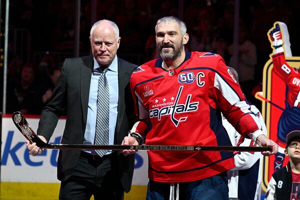 Brian MacLellan, president of Washington Capitals hockey operations, left, poses with Capitals left wing Alex Ovechkin, right, after gifting him a gold stick as part of a ceremony to honor him for scoring 895 career NHL goals before an NHL hockey game against the Carolina Hurricanes, Thursday, April 10, 2025, in Washington. (AP Photo/Nick Wass)
