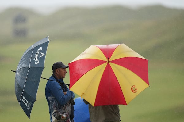 Spectators take cover under an umbrellas as play is suspended due to a thunderstorm waring during a practice round for the 2025 British Open golf championship at the Royal Portrush Golf Club, Northern Ireland, Monday, July 14, 2025. (AP Photo/Francisco Seco)