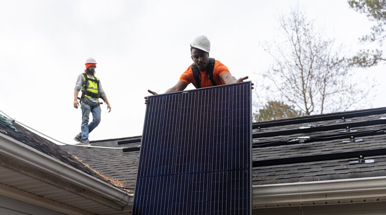 Joe McClain, left, and Mike Harris, right, installers for Creative Solar USA, move solar panels onto the roof of a home in Ball Ground, Georgia on December 17th, 2021.   (Nathan Posner for The Atlanta Journal-Constitution)