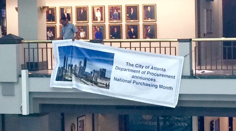 A worker at Atlanta City Hall hangs a banner promoting March as National Purchasing Month. J. Scott Trubey/strubey@ajc.com