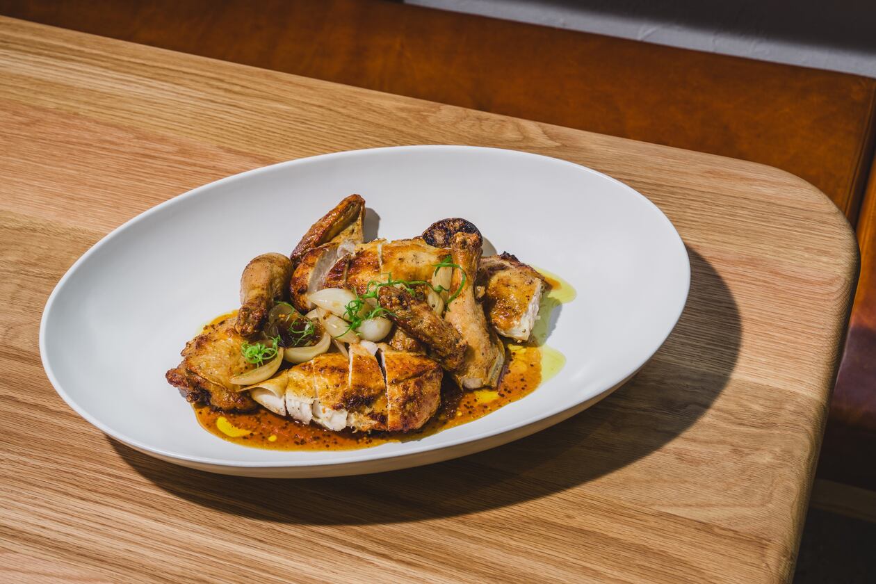 A whole chicken in a large platter on a pale restaurant table, cut up into pieces for easy service.
