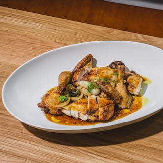 A whole chicken in a large platter on a pale restaurant table, cut up into pieces for easy service.