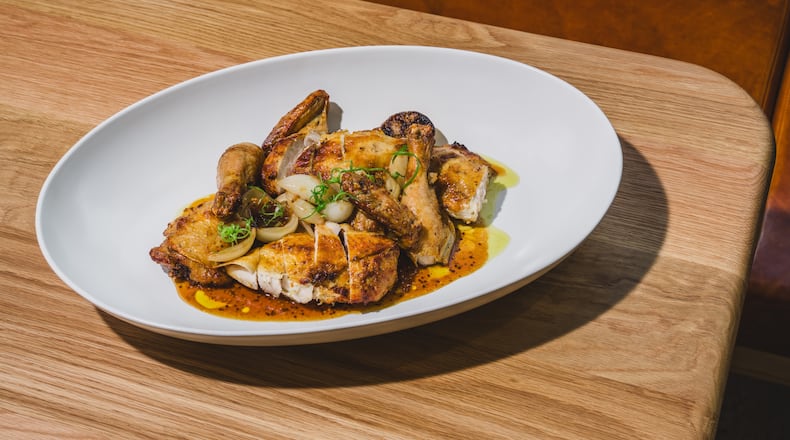 A whole chicken in a large platter on a pale restaurant table, cut up into pieces for easy service.