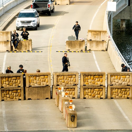 Coast Guardsmen stand watch behind a barrier at Coast Guard Base Alameda on Friday, Oct. 24, 2025, in Oakland, Calif. The barrier was erected earlier in the day after law enforcement officers fired on a vehicle as it backed towards them. (AP Photo/Noah Berger)