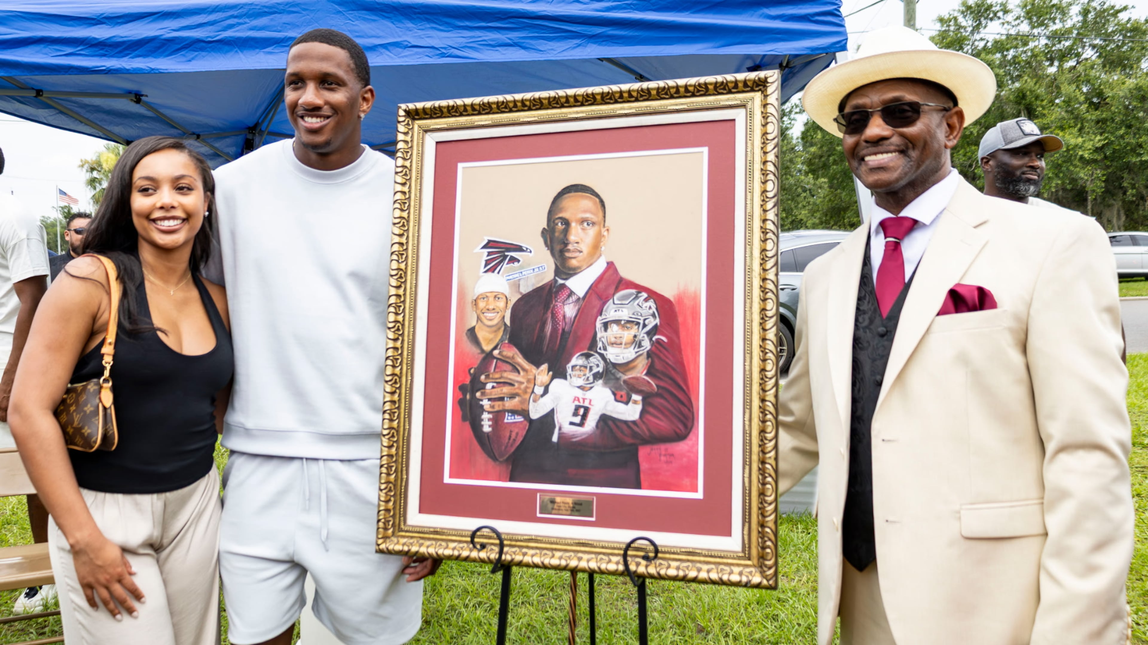 Dade City, Florida, artist Jerry Farmer (right) presents a painting to Falcons quarterback Michael Penix Jr. and his fiancee' Olivia Carter at a street-naming ceremony in Dade City on June 28, 2025. (Photo by Hanna Fox Maglio)