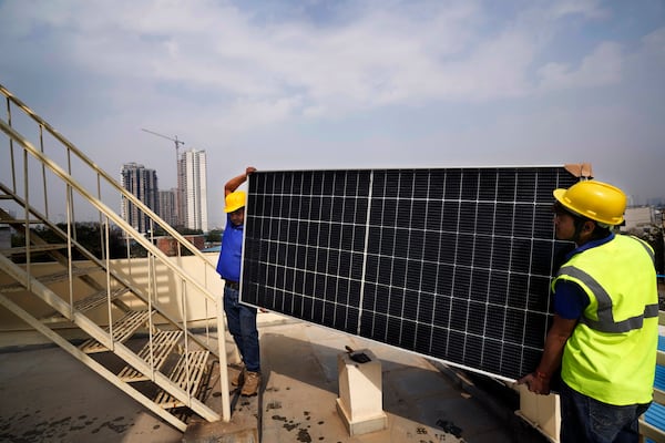 FILE - Workers of Solar Square carry a panel on the rooftop of a residence in Gurugram on the outskirts of New Delhi, India, Feb. 20, 2024. (AP Photo/Manish Swarup, File)