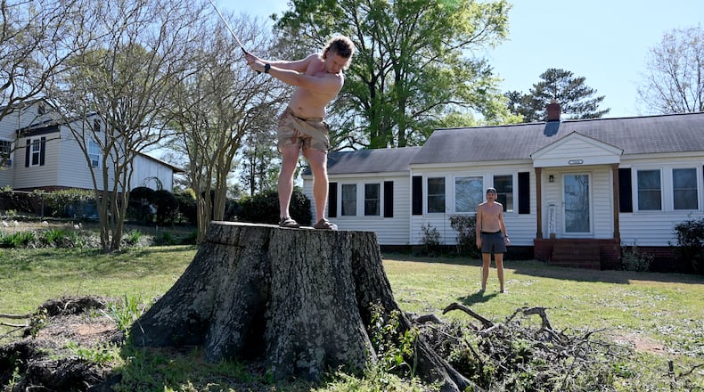 Obie Brannon hits a shot from a tree stump left behind by Hurricane Helene as Walt Steward looks on Tuesday, March 25, 2025. The two are students at the Dental College of Georgia. Their front yard lies about a mile from Augusta National Golf Club. (Hyosub Shin / AJC)
