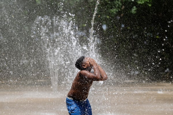 A child covers his face while a stream of water pours down at Waterfront Park on Sunday, June 22, 2025, in Louisville, Ky. (AP Photo/Jon Cherry)