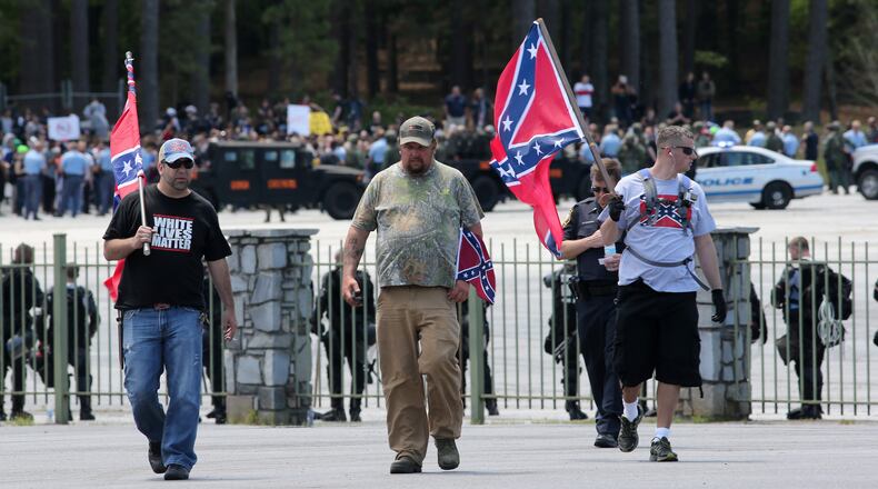 Joseph Andrews, from left, of Woodstock, Shaun Winkler of Mississippi and James Berry of Michigan walk through a designated protest area in support of the Confederate battle flag, as hundreds of counter-protesters can be seen 100 yards behind them at Stone Mountain Park on a Saturday afternoon in April. Ben Gray,bgray@ajc.com