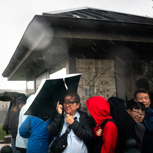 Visitors take cover during heavy rain near the U.S. Capitol on Capitol Hill in Washington, Monday, March. 16, 2026. (AP Photo/Nathan Howard)
