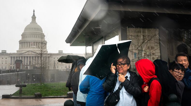 Visitors take cover during heavy rain near the U.S. Capitol on Capitol Hill in Washington, Monday, March. 16, 2026. (AP Photo/Nathan Howard)