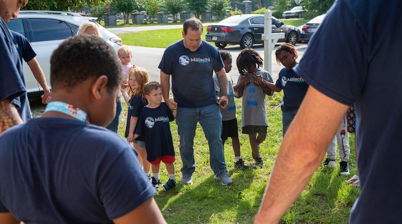 Pastor Terrell Scott (center) prays for volunteers with the Malachi Project before they go out to serve neighbors in the McDonough Housing Authority Complex. PHIL SKINNER FOR THE AJC