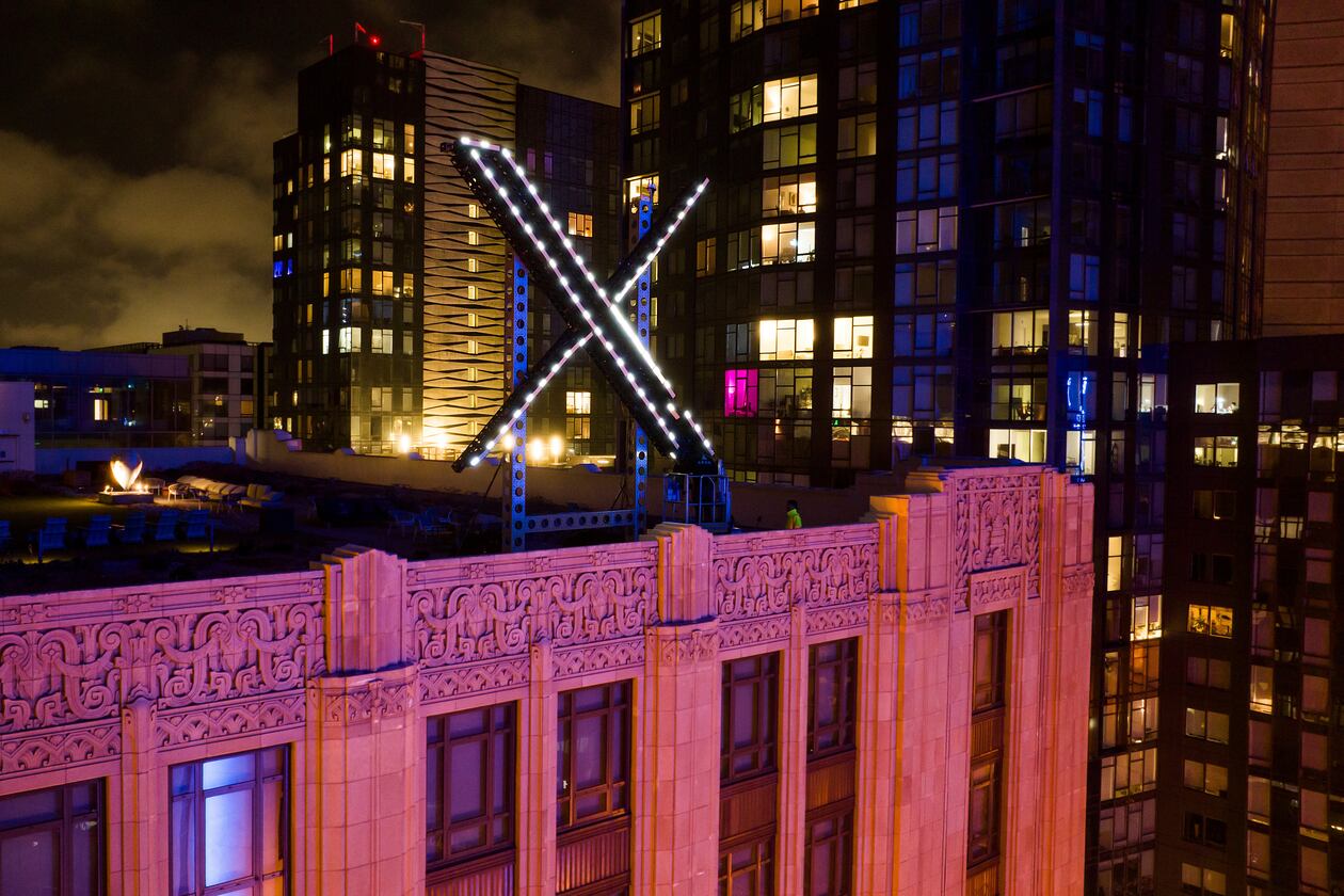 Workers install lighting on an "X" sign atop the company headquarters formerly known as Twitter in downtown San Francisco. X is owned by Elon Musk, who also owns the AI tool Grok, which has been scrutinized for its unrestricted creation of AI-generated nude images, including of adolescents and children. (AP 2023)