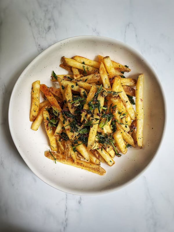 A plate of french fries garnished with crispy greens is plated and shown on a marble table top.