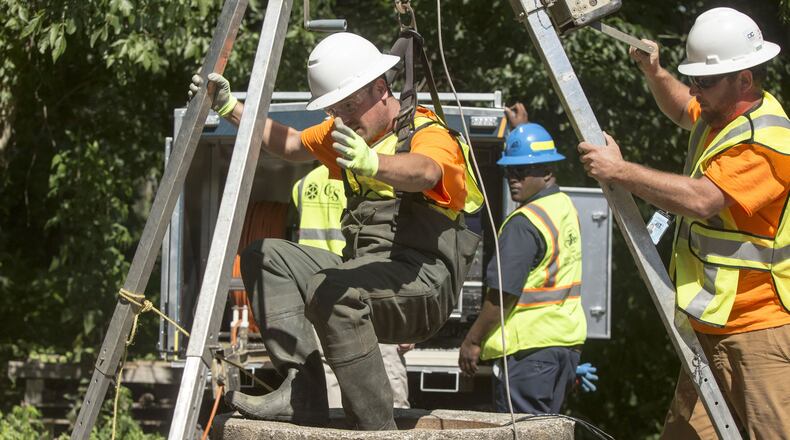 Workers pulled a crew member through a manhole after lowering him into DeKalb County’s sewer system to inspect sediment build-up. Chad Rhym/ Chad.Rhym@AJC.com