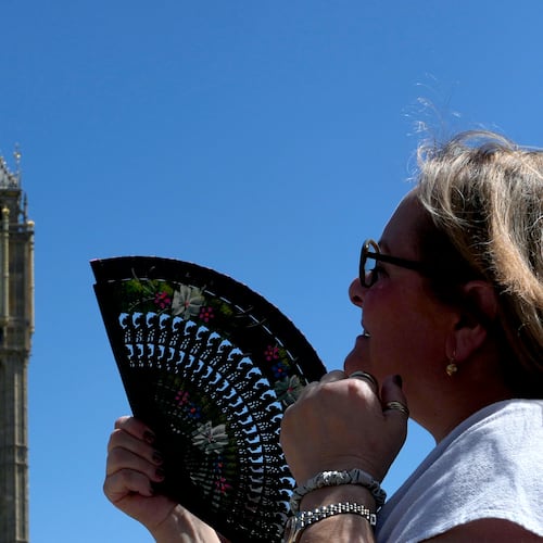 FILE - A woman cools herself outside the Palace of Westminster in London, May 26, 2026. (AP Photo/Kin Cheung, File)