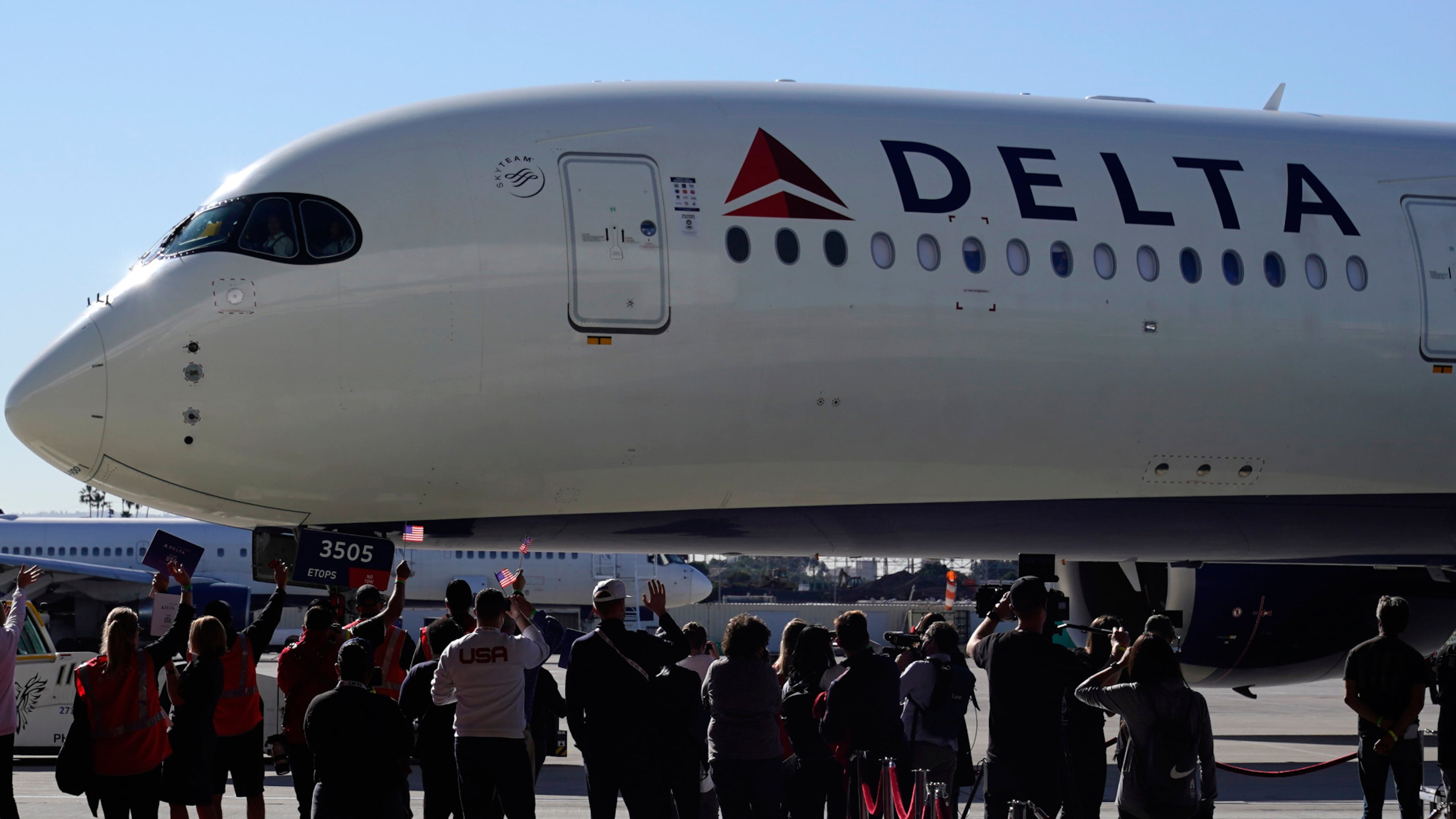 This photo combination shows an Aeromexico plane as it is prepared for a flight from Renton Municipal Airport, in Renton, Wash., Nov. 18, 2020 and Delta Airlines employees waving flags at a Delta Airlines terminal, Jan. 27, 2022, in Los Angeles. (AP Photo/Ted S. Warren, Marcio Jose Sanchez)