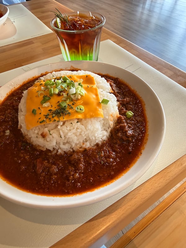 A bowl of braised beef and rice is topped with a slice of American cheese and herbs, with a layered green apple cold brew drink behind it.