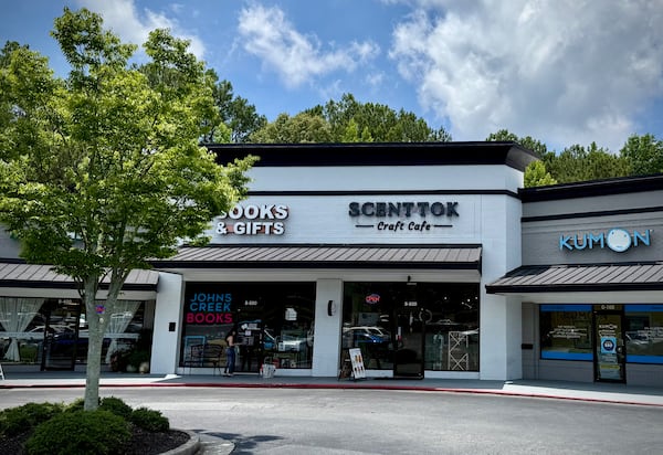 A photo of several shops in a strip mall with the focus on one storefront with a sign reading ScentTok Craft Cafe