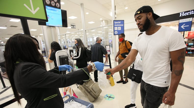 A Hartsfield-Jackson Airport staff person hands out face masks to passengers entering the security line in the airport’s South Terminal. Tuesday, June 23, 2020. Miguel Martinez for The Atlanta Journal-Constitution