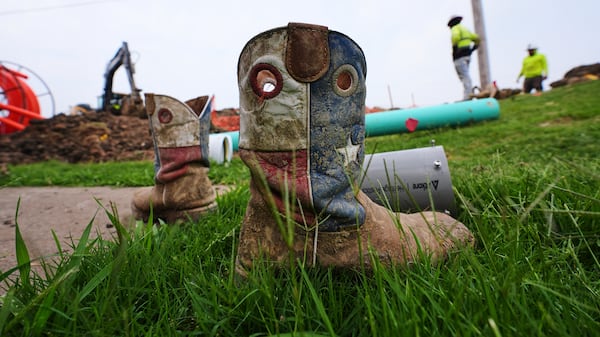 A worker's Texas themed boots sit in the grass as a crew works laying fiber optic cable in Princeton, Texas, Friday, May 16, 2025. (AP Photo/LM Otero)