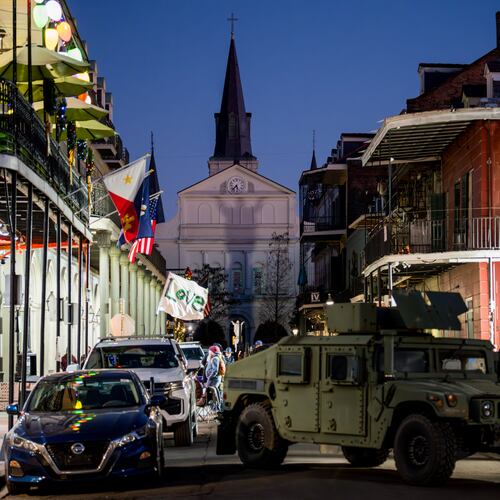 A man walking on Bourbon Street holds a flag reading "Love" as an armored vehicle sits parked on a street in the French Quarter as part of a National Guard deployment for New Year's celebrations in New Orleans, Tuesday, Dec. 30, 2025.