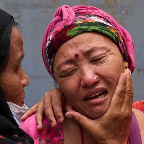 Relatives comfort Jantari Gurung, whose husband is missing, as she looks at photographs of people killed in flash floods displayed outside a government hospital in Kathmandu, Nepal, Sunday, Aug. 30, 2026. (AP Photo/Dar Yasin)