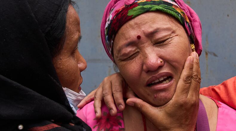 Relatives comfort Jantari Gurung, whose husband is missing, as she looks at photographs of people killed in flash floods displayed outside a government hospital in Kathmandu, Nepal, Sunday, Aug. 30, 2026. (AP Photo/Dar Yasin)