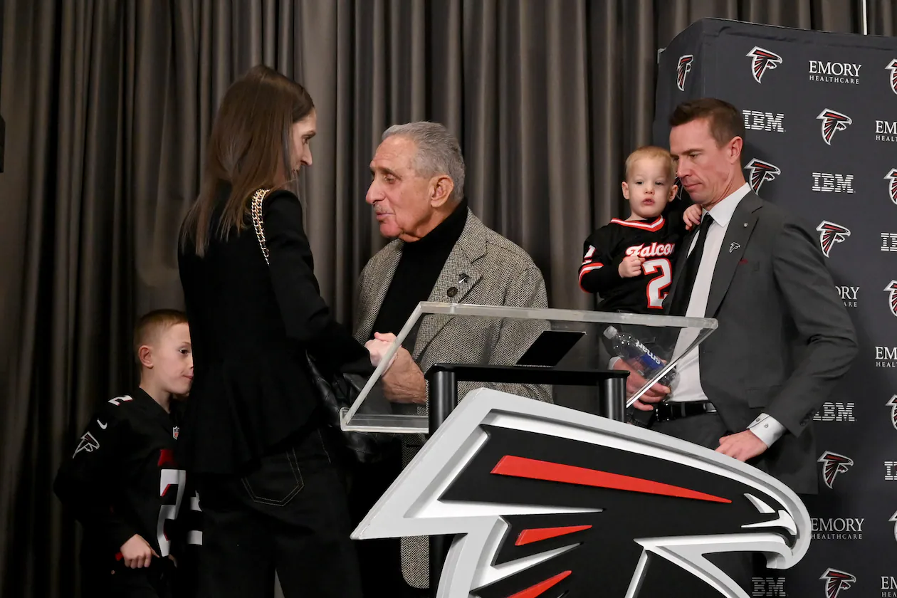 Atlanta Falcons owner Arthur M. Blank (center) holds the hand of Sarah Ryan, wife of Matt Ryan (right), as the new Atlanta Falcons president of football holds his son, Cal, after a news conference Tuesday, Jan. 13, 2026, in Flowery Branch. (Hyosub Shin/AJC)