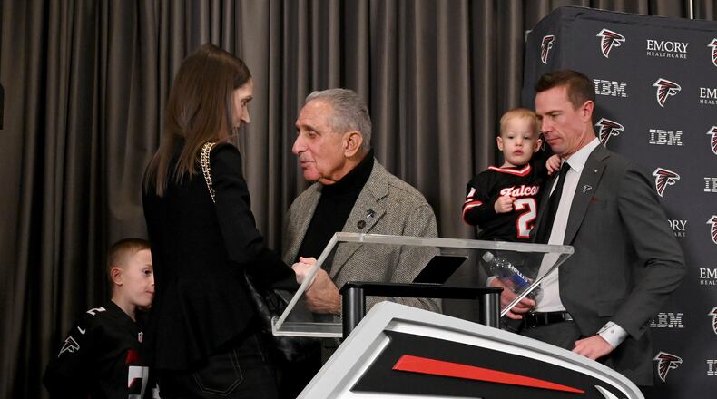 Atlanta Falcons owner Arthur M. Blank (center) holds the hand of Sarah Ryan, wife of Matt Ryan (right), as the new Atlanta Falcons president of football holds his son, Cal, after a news conference Tuesday, Jan. 13, 2026, in Flowery Branch. (Hyosub Shin/AJC)