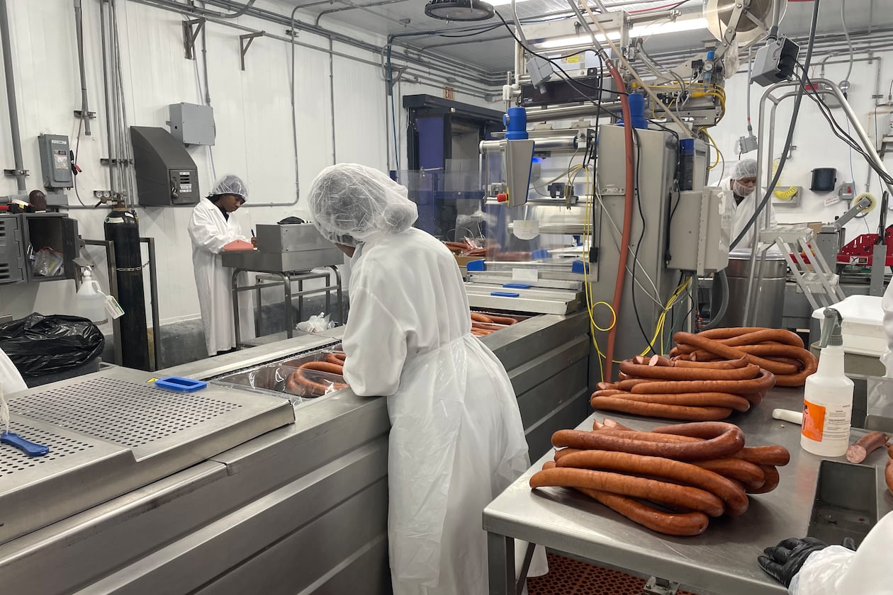 Factory workers in white food safety gear process sausage
