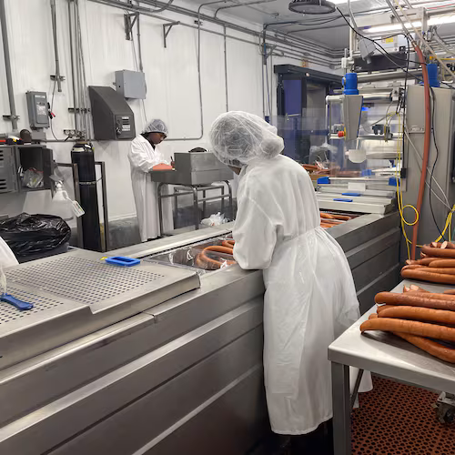 Factory workers in white food safety gear process sausage