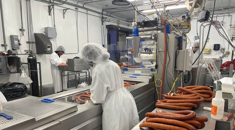 Factory workers in white food safety gear process sausage