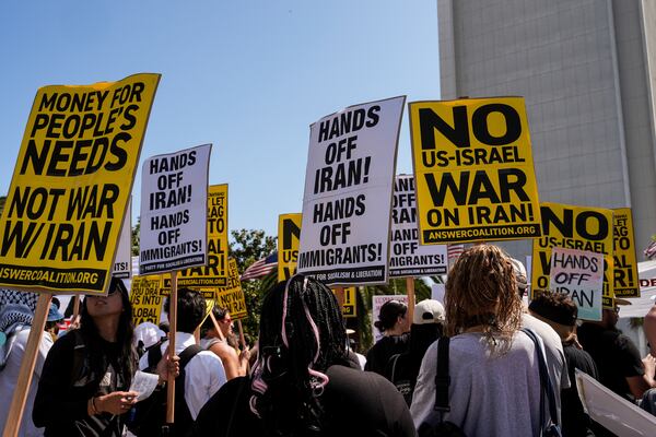 Two anti-war demonstrators hold signs outside the Wilshire Federal Building in Los Angeles Sunday, June 22, 2025, following U.S. airstrikes on Iran's nuclear facilities. (AP Photo/Jae C. Hong)