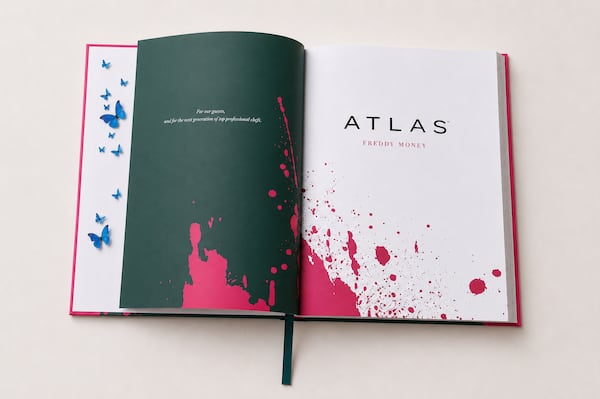 The "Atlas" cookbook lays open to the title page with hot pink paint splatters and blue butterflies dotting its pages.